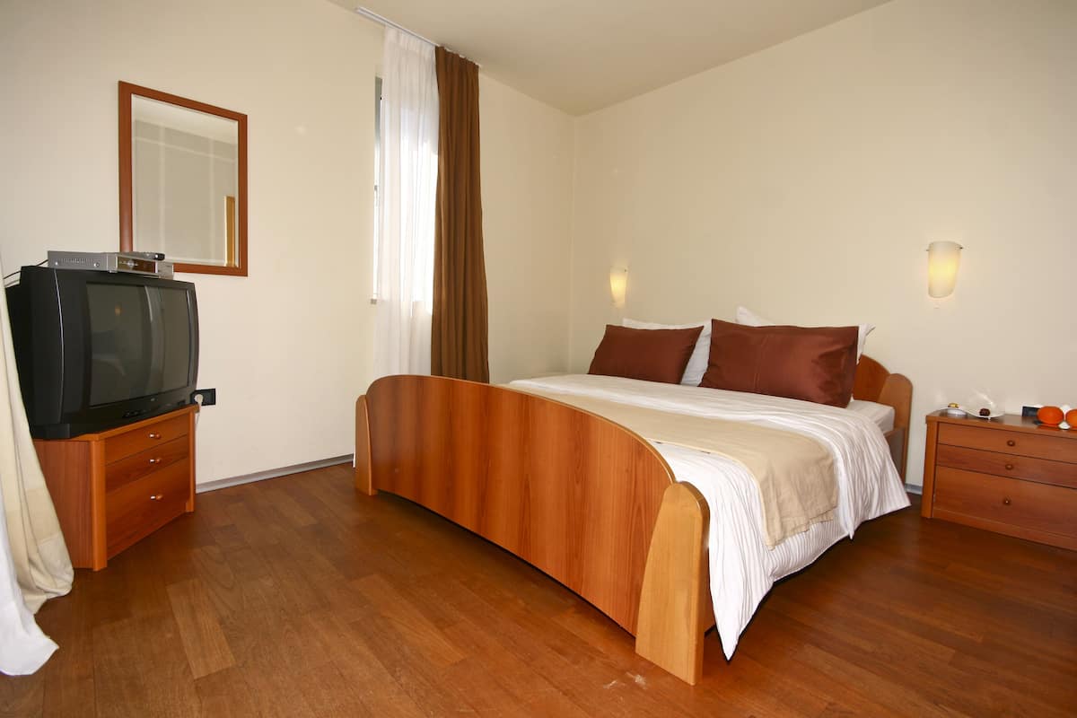 A bedroom with a wooden bed, a television on a wooden dresser, and a mirror on the wall.