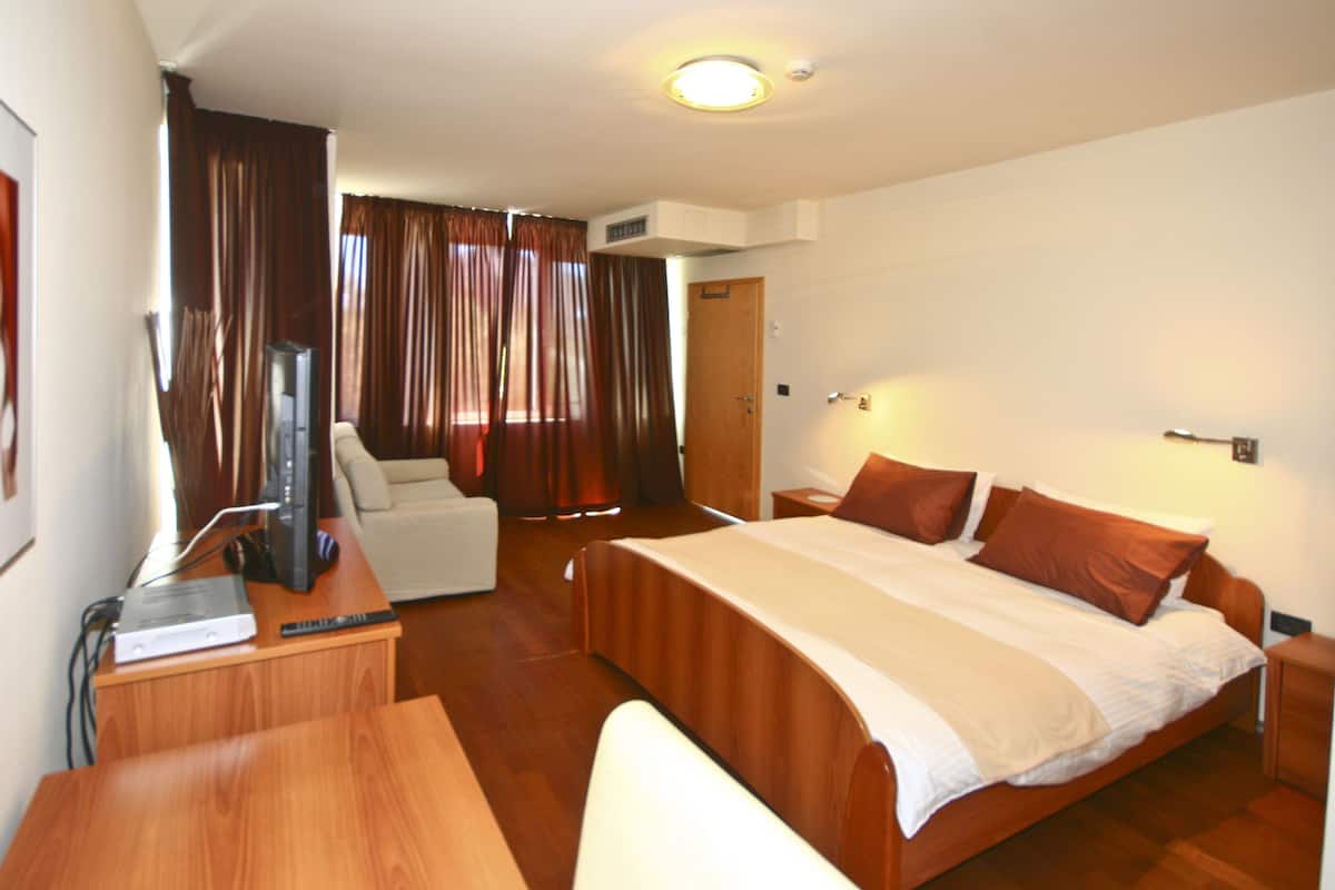 A hotel room with a bed, a desk, a chair, a television, and curtains.