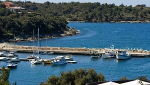 A marina with various boats docked, surrounded by a rocky coastline and dense forest. - Villa Feniks (Medulin)