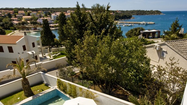A rooftop pool area with lounge chairs and umbrellas, overlooking a coastal town and the sea. - Villa Feniks (Medulin)