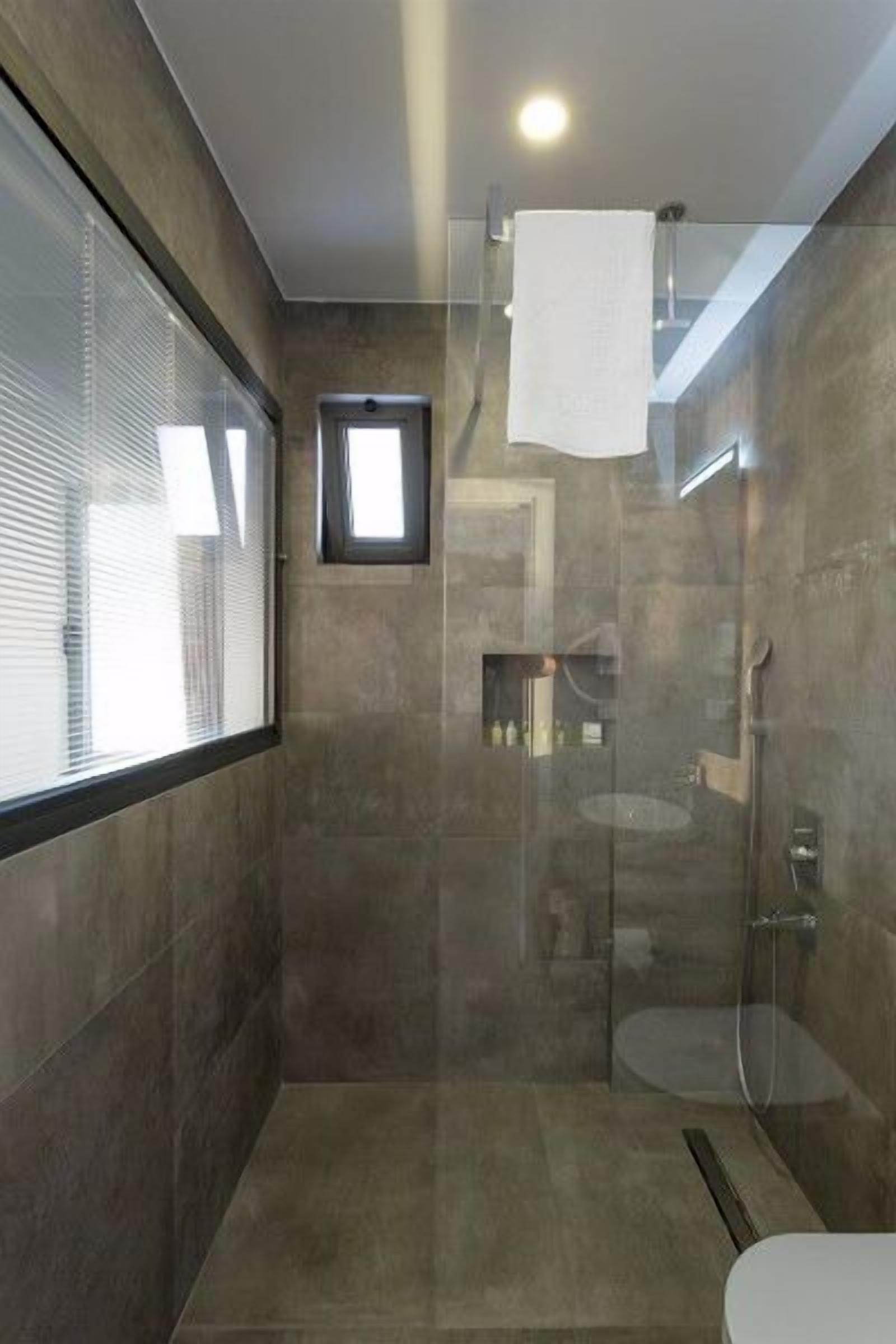 Un baño moderno con cabina de ducha de vidrio, un ventanal pequeño y una toalla colgada en la pared.
