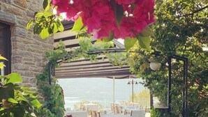 An outdoor dining area with tables and chairs, surrounded by lush greenery and a stone wall. - Aria Butik Otel (Marmaris)