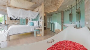 A modern bedroom with a large bed, a white canopy, a bathtub with rose petals, and a bathroom with a large mirror and sink. - TreeHouse Villas Koh Yao - Adults Only (Ko Yao)
