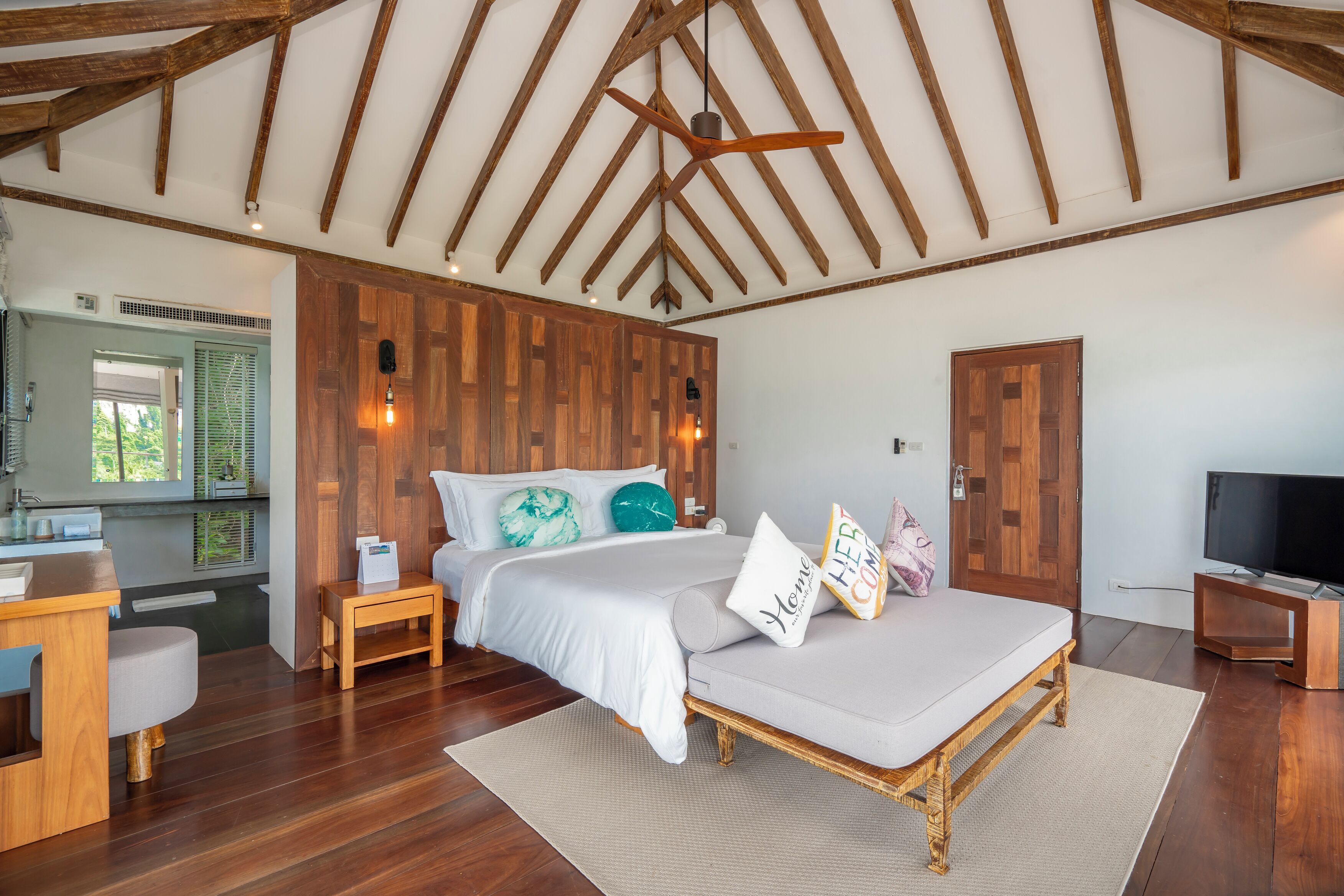 A bedroom with a wooden ceiling, a bed with white bedding, a wooden nightstand, a TV stand, and a window with blinds.