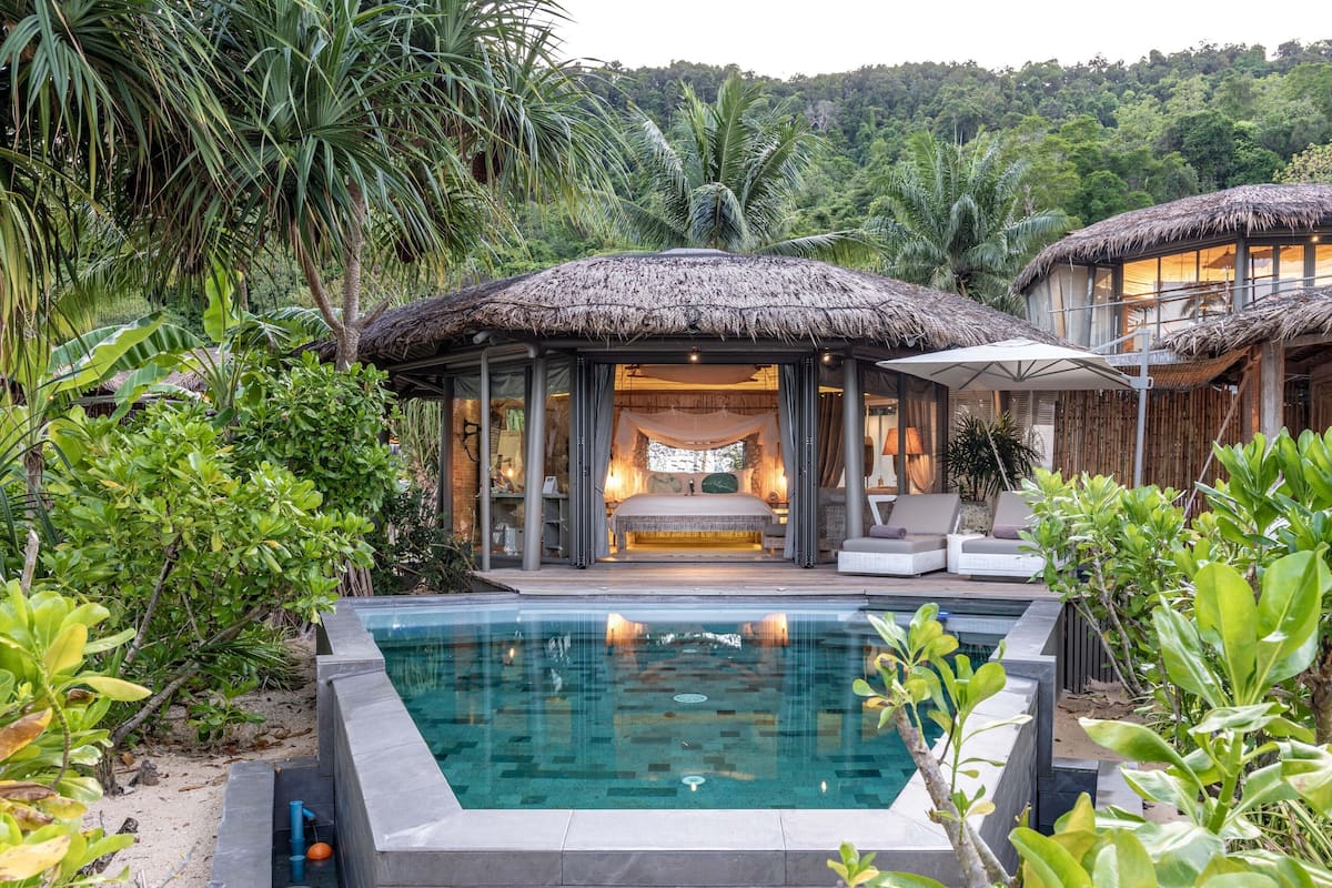 A resort with a pool, thatched-roof structures, and lush greenery.
