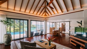 A spacious living area with a large window offering a view of the sea, a wooden ceiling, and a modern entertainment unit. - TreeHouse Villas Koh Yao - Adults Only (Ko Yao)