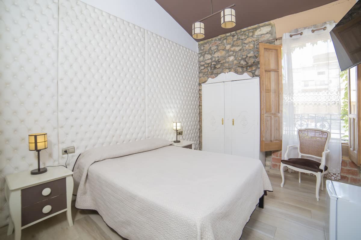 A bedroom with a bed, nightstands, a wardrobe, a chair, and a balcony with a view.