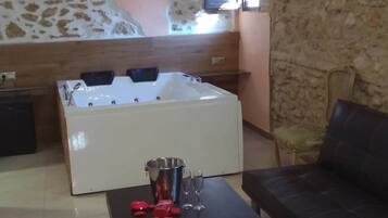 Una habitación con una bañera grande, un sofá negro y una mesa de centro de vidrio transparente con adornos rojos.