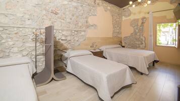 A room with two beds, a stone wall, and a window with a view.