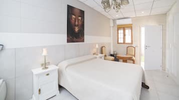 Quarto moderno com cama grande, mesas de cabeceira, uma cadeira e porta que dá para outro espaço.