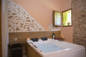 A bathroom with a large bathtub, a stone wall, and a window with a view of greenery.