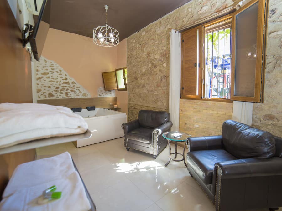 Una habitación acogedora con pared de piedra, una bañera, dos sofás de cuero y una pequeña mesa redonda.