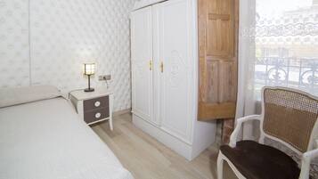 Un dormitorio con una cama, una mesita de noche con lámpara, un armario y una silla.