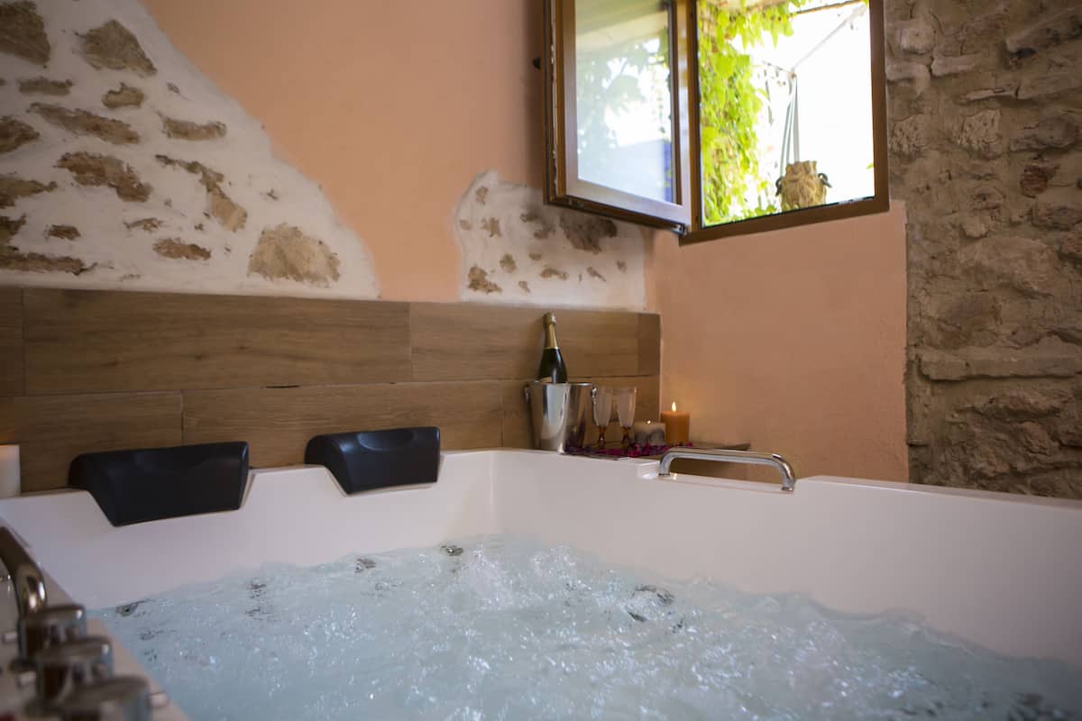 A modern bathroom with a large bathtub, wooden headboard, and a stone wall.