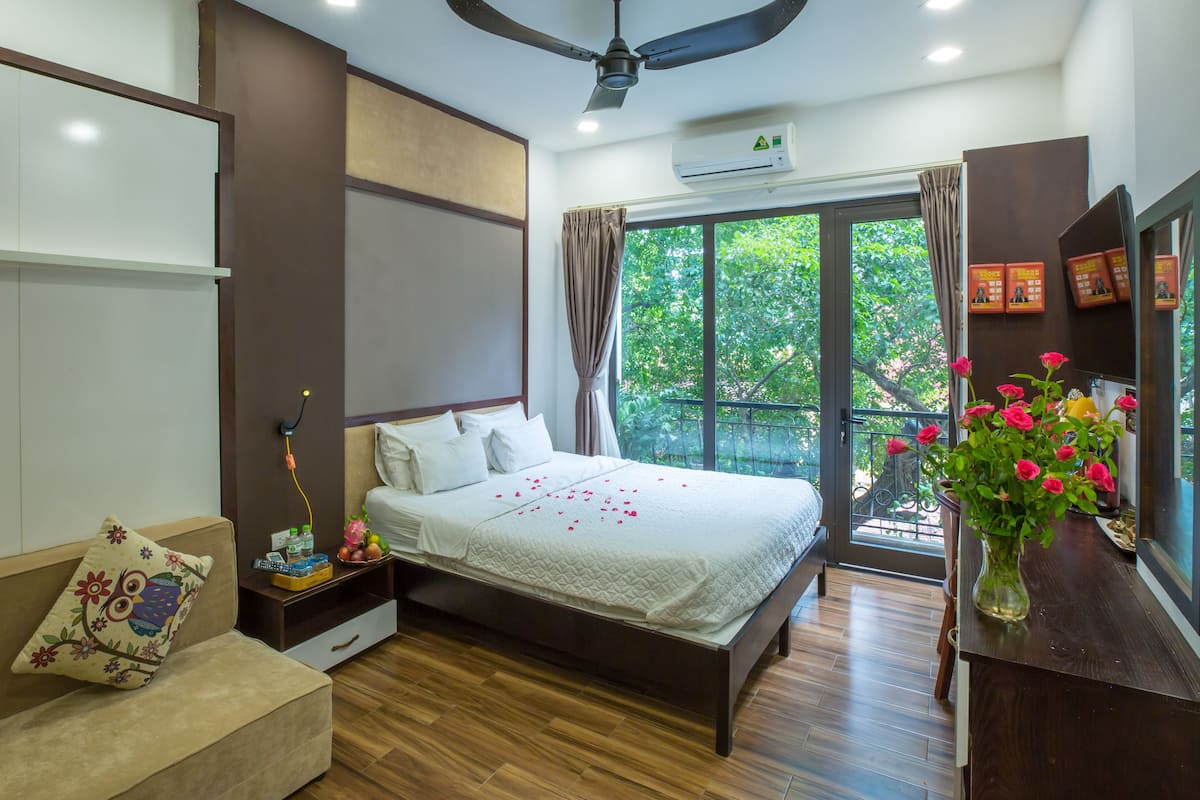 A bedroom with a bed, bedside table, and a window with a view of greenery.