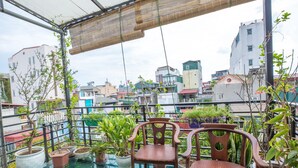 Ein Balkon mit Topfpflanzen, zwei Holzstühlen und einem Glastisch.