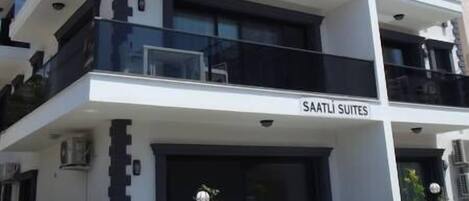 A modern multi-story building with balconies, labeled "SAATLI SUITES."