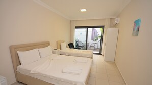 A hotel room with two beds, a desk, and a view of the outdoor area.