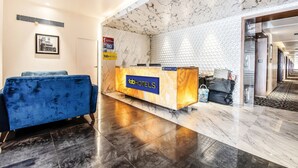 A hotel reception area with a marble wall, a reception desk, and a blue sofa. - FabHotel High Rise Suites (Bengaluru)