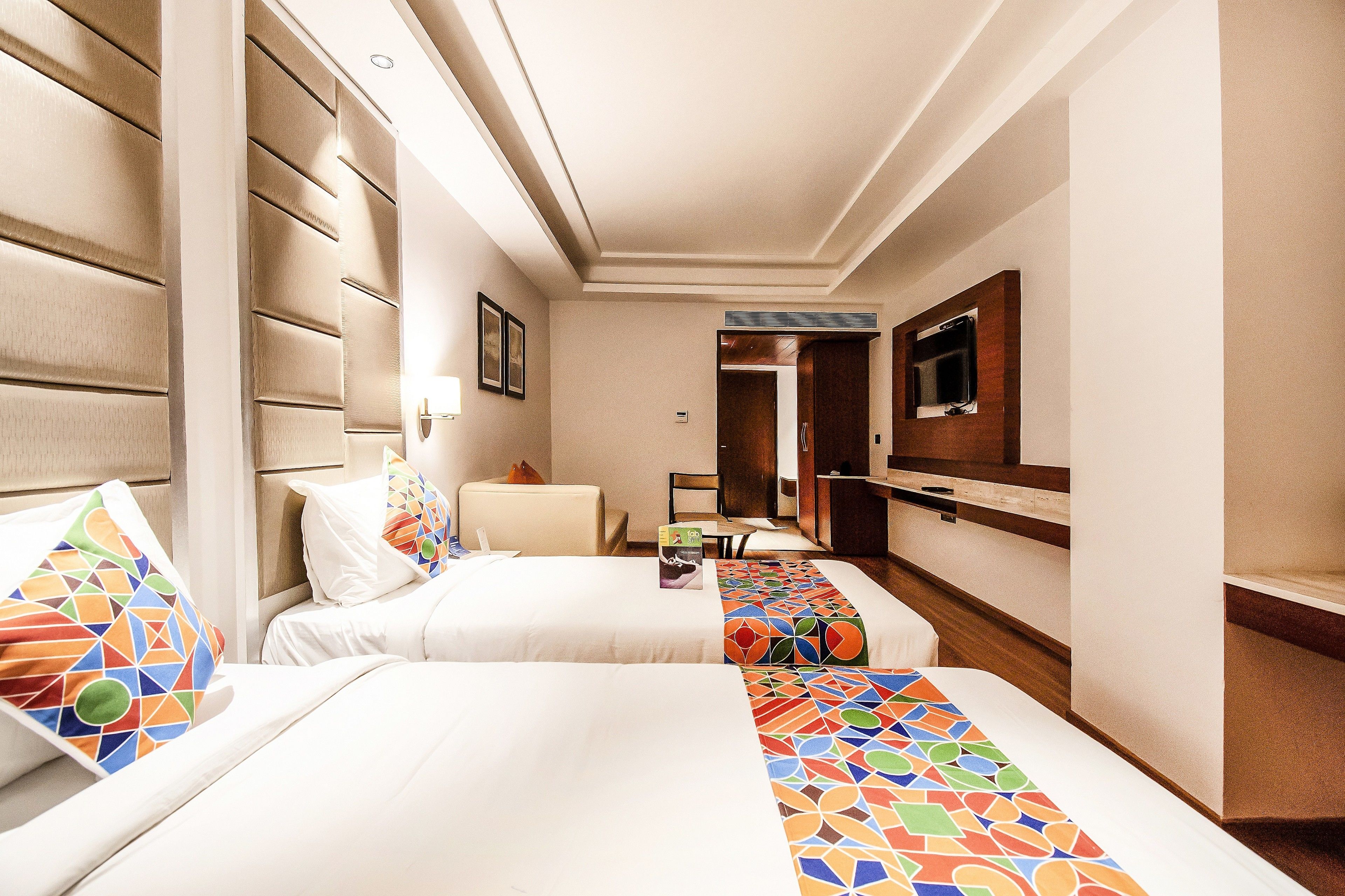 Quarto de hotel com duas camas, uma escrivaninha, uma cadeira, uma televisão e a porta do banheiro.