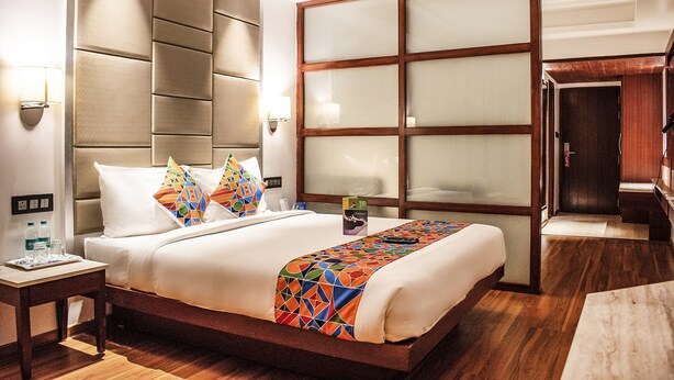 A hotel room with a large bed, a wooden headboard, a large window, and a wooden wardrobe. - FabHotel High Rise Suites (Bengaluru)