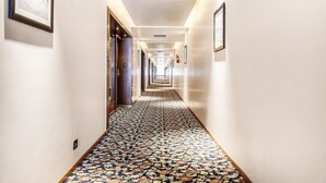 A long, narrow hallway with patterned flooring and framed pictures on the walls. - FabHotel High Rise Suites (Bengaluru)