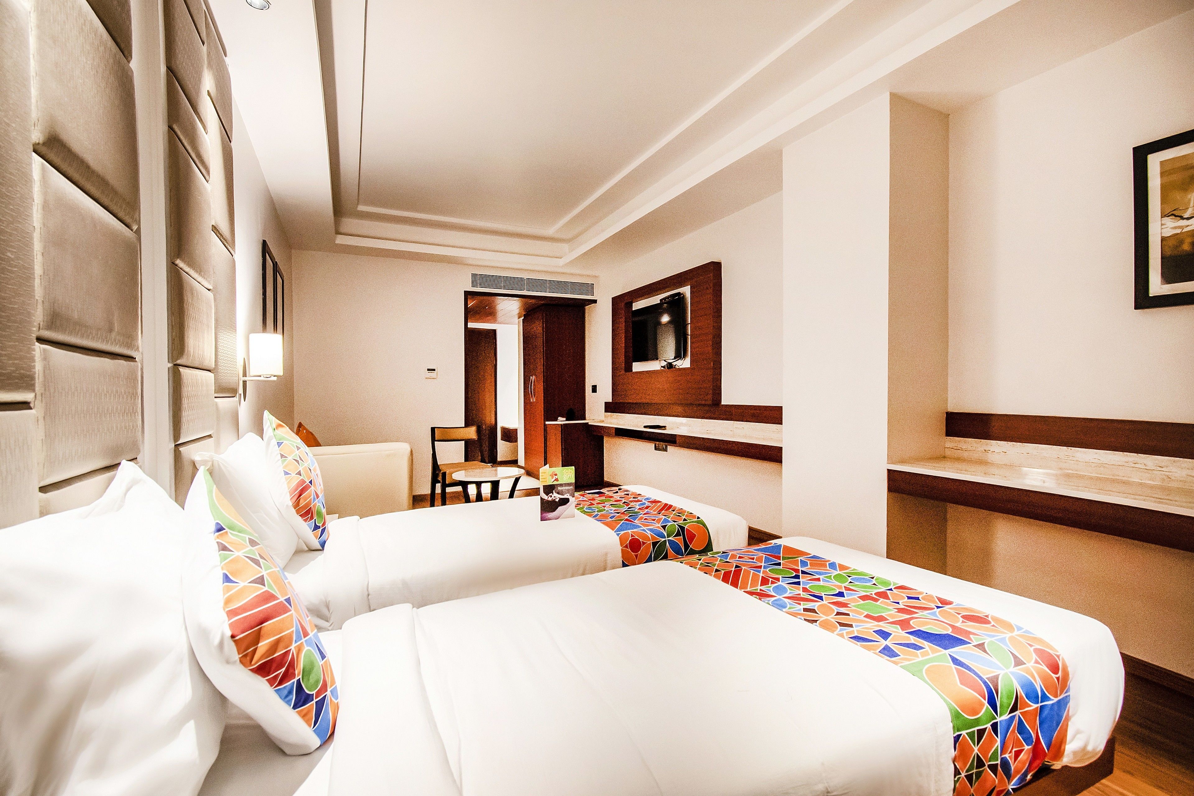 A hotel room with two beds, a desk, a chair, a TV, and a bathroom.