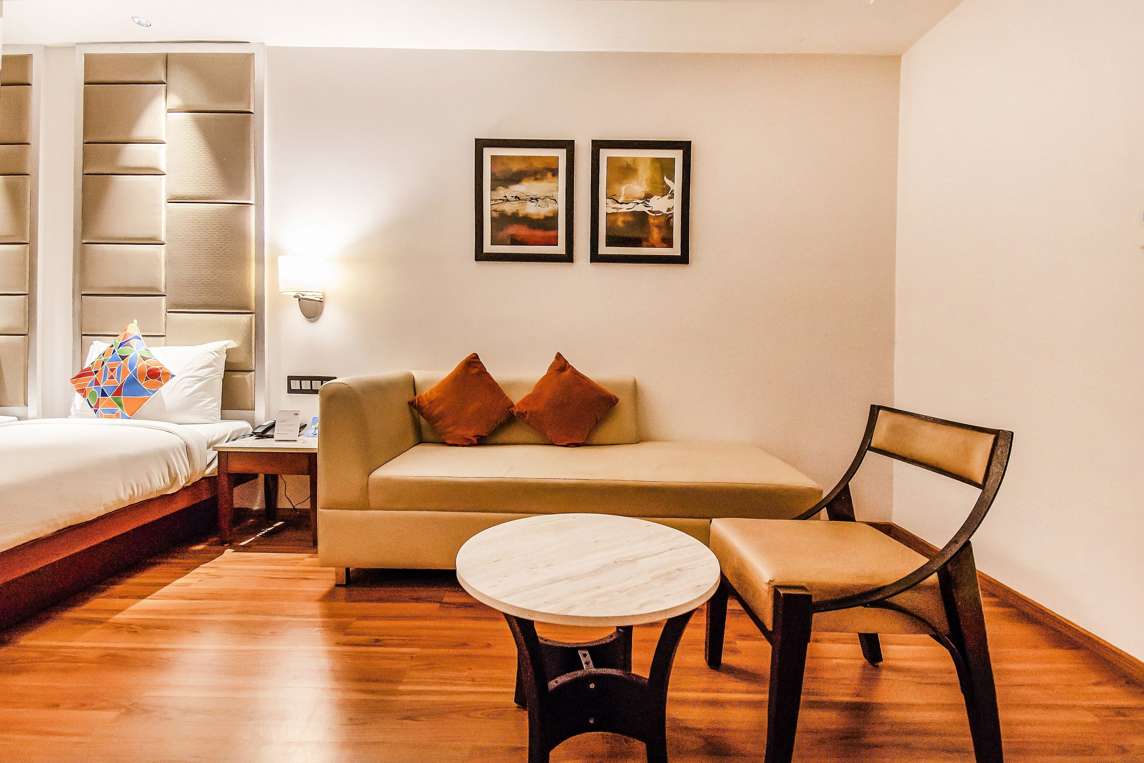 A hotel room with a bed, a sofa, a chair, a small table, and two framed pictures on the wall.