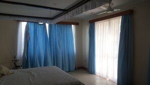 Un dormitorio con cama, ventilador de techo y ventanas amplias con cortinas azules.