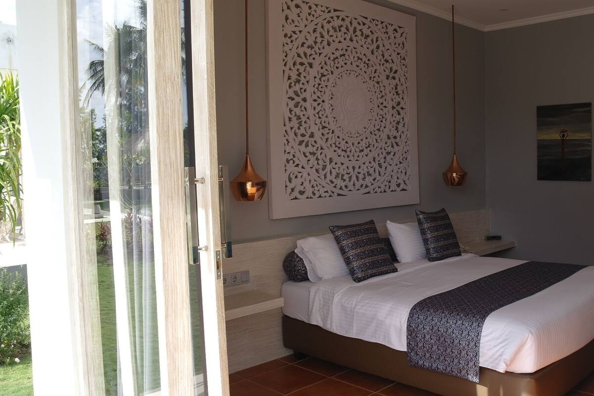 A bedroom with a bed, pillows, a wall-mounted decorative panel, and a painting.