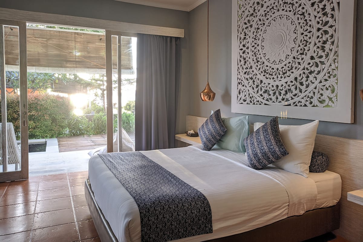 A bedroom with a large bed, a view to the outside, and a decorative wall piece.