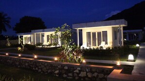 Een modern hotel met een goed verlichte gevel, voorzien van een kiezelpad en verzorgde beplanting.