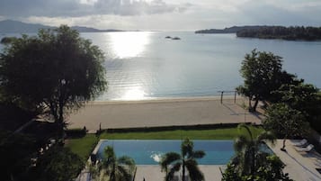 A beach view with a pool and lounge chairs.