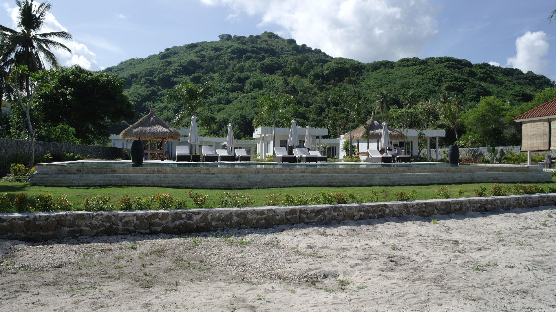 Ein Resort mit Poolbereich, Liegestühlen und einer Struktur mit Reetdach.