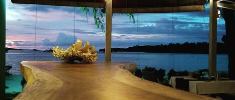A wooden pathway leading to a seating area with a view of a body of water and a sunset.
