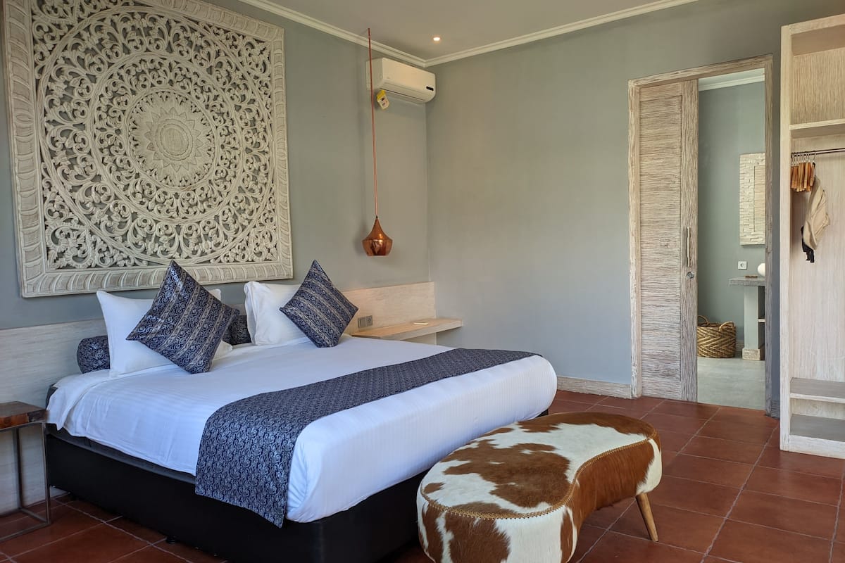 A bedroom with a large bed, decorative wall panel, and a hanging lamp.
