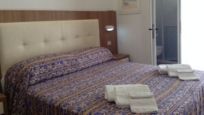 Una cama bien hecha con una colcha estampada, una mesita de noche con una lámpara y una puerta que da a un baño.