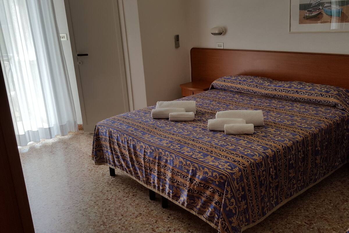 A bedroom with a patterned bedspread, a wooden headboard, and a framed picture on the wall.