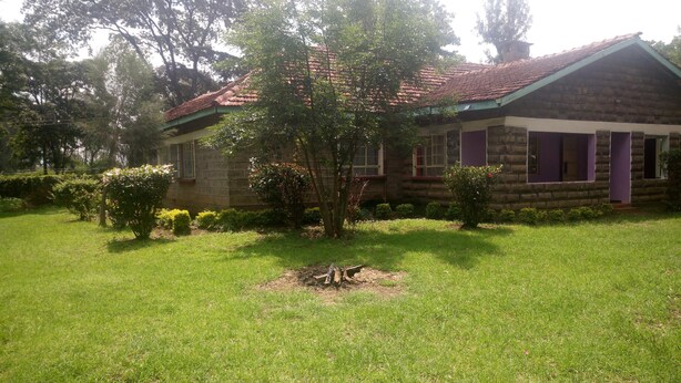 A stone building with a red-tiled roof, surrounded by a well-maintained lawn and various shrubs. - Hudsons Guest House (Nakuru)