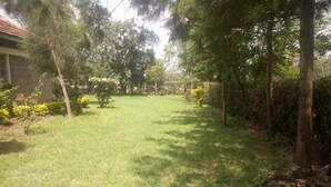 A grassy yard with trees and a stone building. - Hudsons Guest House (Nakuru)