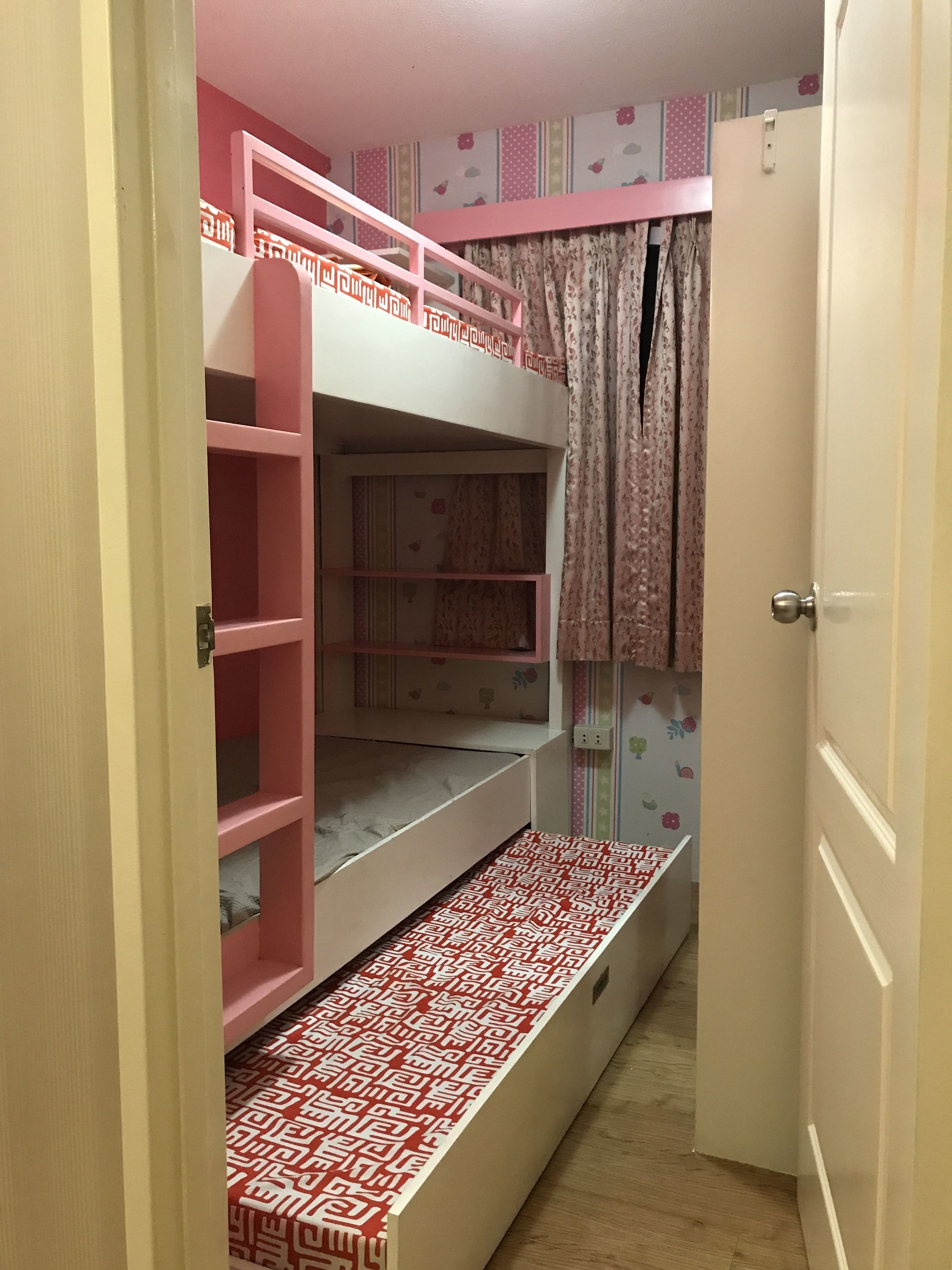 Un lit superposé avec une literie rose et blanche, un sol à motifs et une porte avec un rideau.