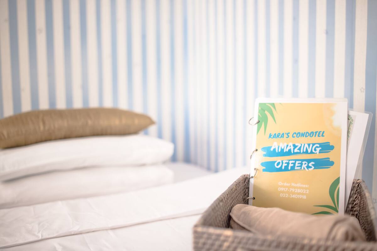 A brochure titled "KARA'S CONDOLET AMAZING OFFERS" placed on a bed with white bedding and a single beige pillow.