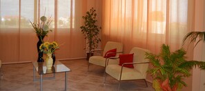 Ein modernes Wohnzimmer mit einem Glastisch, einem beigefarbenen Sofa mit roten Kissen und einer Zimmerpflanze.