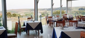 Ein Restaurant mit Terrassensitzgelegenheiten, Tische sind mit weißen und blauen Tischdecken bedeckt, und es bietet einen malerischen Ausblick auf die Landschaft.