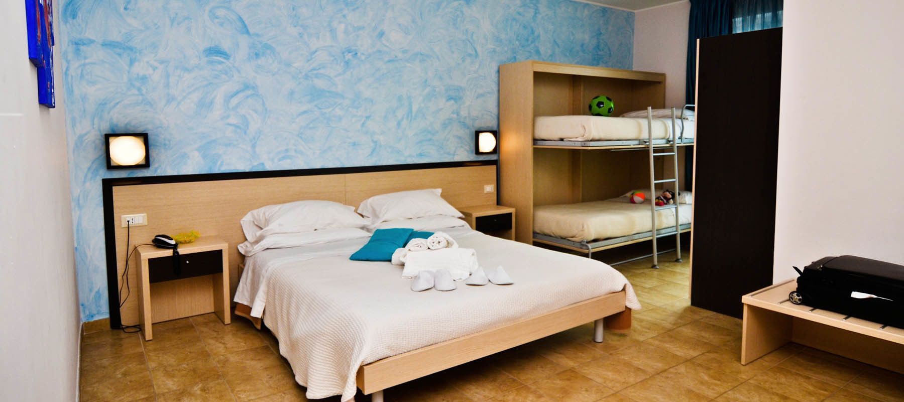Una camera d'albergo con un letto grande, una scrivania, un armadio e un letto a castello.