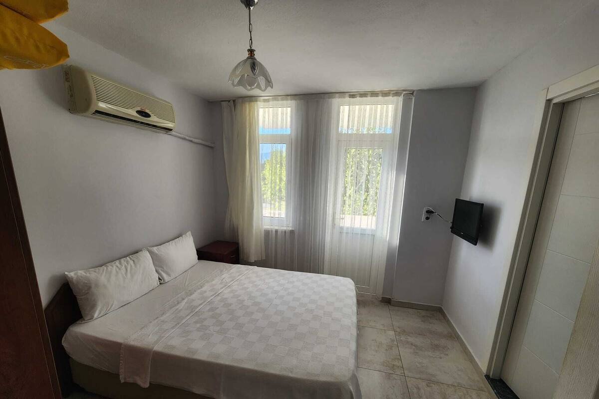 A bedroom with a bed, a ceiling fan, a TV, and a window with curtains.