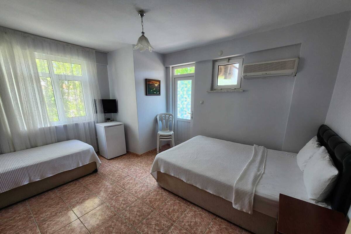 A bedroom with a bed, a small desk, a chair, a television, and a window.
