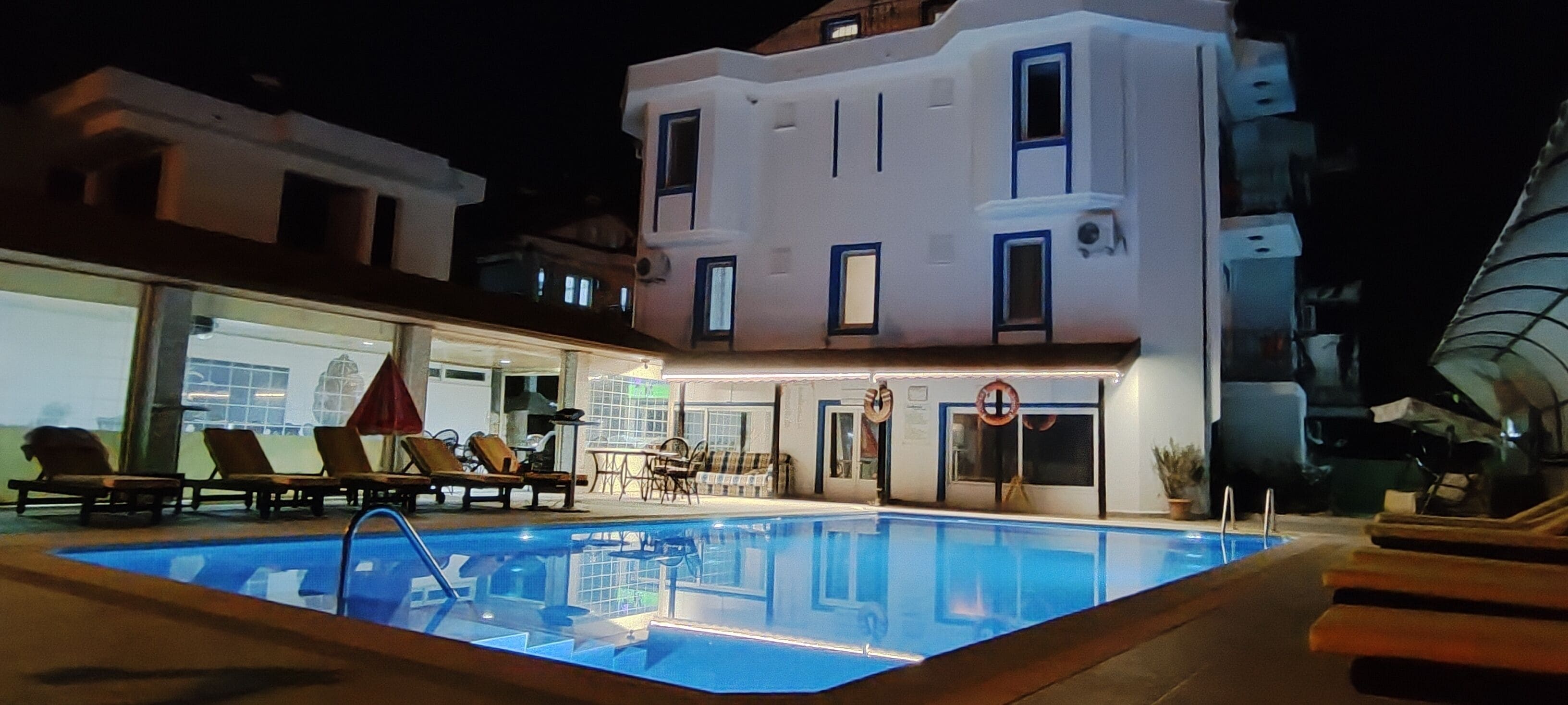 A swimming pool with lounge chairs and a table, surrounded by a building with multiple windows and balconies.