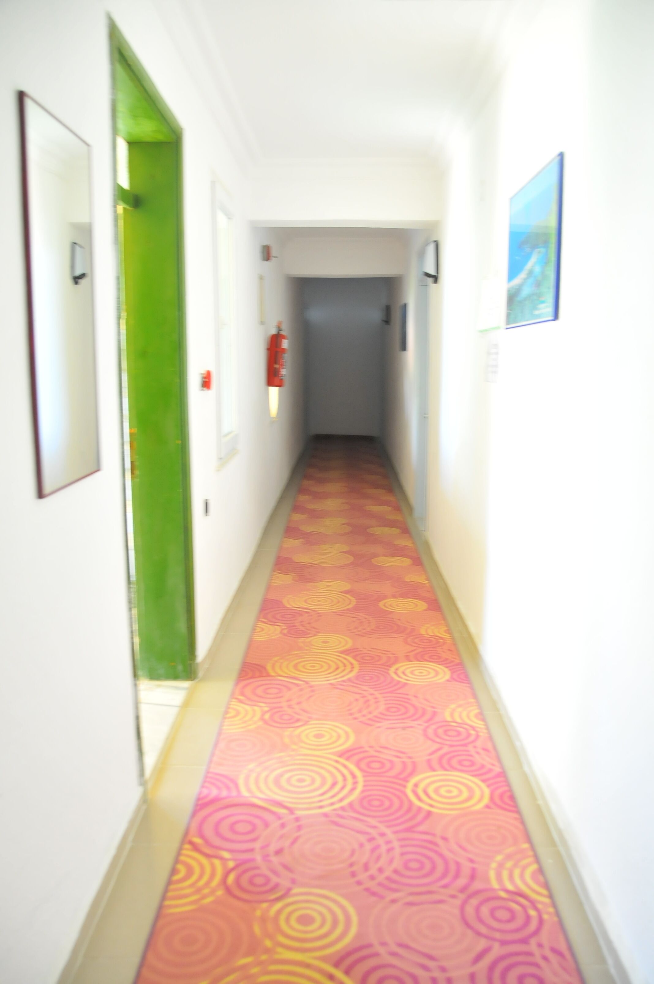 A hallway with a patterned carpet, a green door, and a fire extinguisher on the wall.