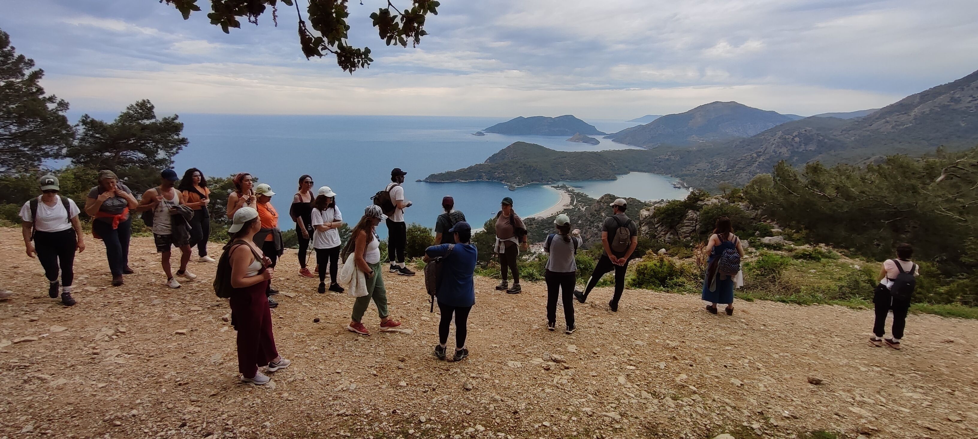 A group of people on a rocky hillside with a scenic view of a coastline and mountains in the distance.